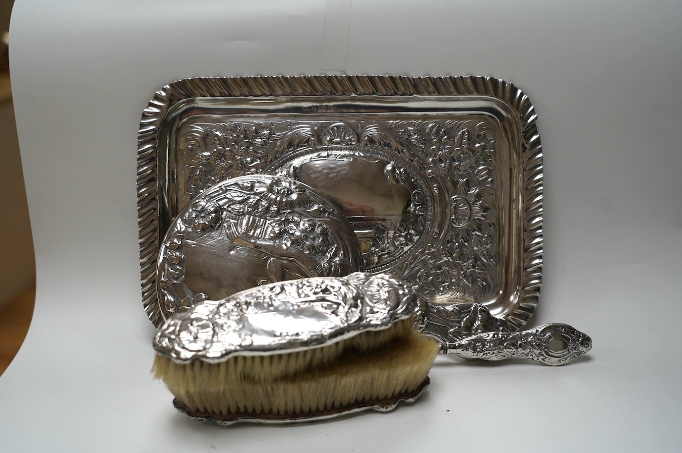 An Edwardian Art Nouveau four piece dressing table set including a tray, Birmingham, 1904, 30.3cm and a similar silver mounted shoe horn. Condition - poor to fair